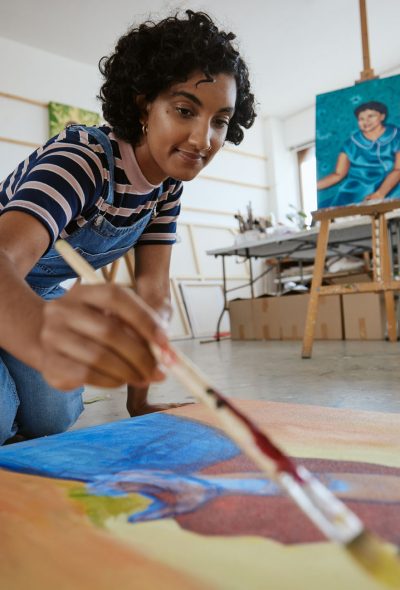 Studio, art and a woman painting on floor in design school with creativity and paint brush. Artist student from India, happy painter and a girl working on creative school project canvas in classroom
